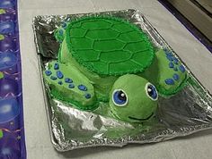 a cake shaped like a turtle sitting on top of a sheet of tin foil covered in green frosting