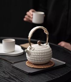 a white teapot sitting on top of a table next to a cup and saucer