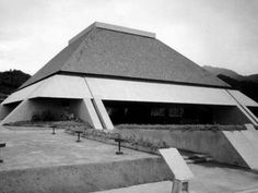 a black and white photo of a triangular building with benches in front of the entrance