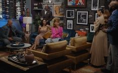 several people in a living room with pictures on the wall and one woman sitting on a couch