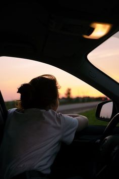 a person sitting in the driver's seat of a car looking out the window