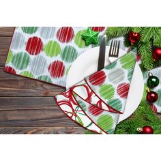 a place setting with green and red napkins, silverware and christmas decorations on a wooden table