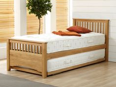 a wooden bed frame with two mattresses and a plant in the corner next to it