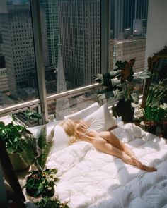 a woman laying on top of a bed in a bedroom next to a large window