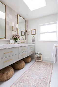 a white bathroom with gold accents and large mirror above the vanity, along with two stools