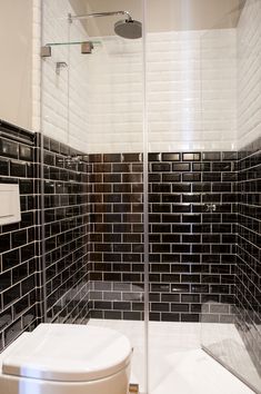 a white toilet sitting next to a shower in a bathroom with black tiles on the walls