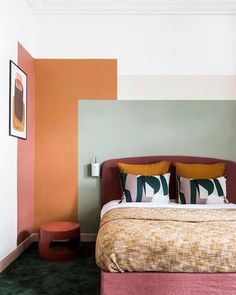 a bed with two pillows on top of it next to a wall painted in different colors