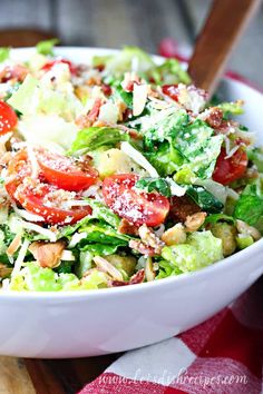 a salad with tomatoes, lettuce and other toppings in a white bowl