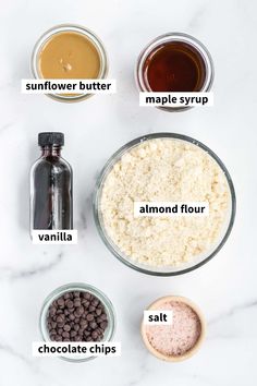 ingredients to make chocolate chip cookies laid out on a white marble counter top, including almonds, salt, butter, maple syrup and vanilla