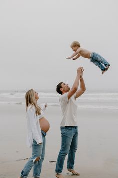 a man holding a baby up in the air while standing next to his pregnant wife