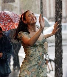 a woman standing under an umbrella in the rain with her hand up to her mouth