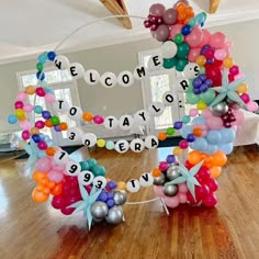 a welcome sign made out of balloons in the middle of a room with wooden floors