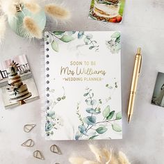 a wedding planner next to other items on a white table with gold pen and photos