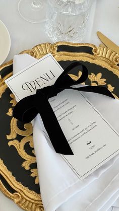 a black and gold plate with a menu on it that has a bow at the top