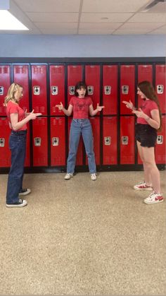 three girls standing in front of red lockers with their hands out to each other