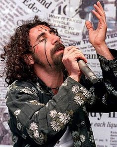 a man with long hair holding a microphone up to his mouth while standing in front of a newspaper wall