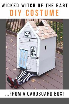 a woman sitting on the ground in front of a cardboard house with her legs crossed