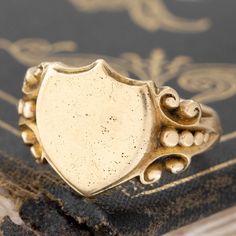 A delicious antique signet ring in 15kt gold, a common metal used for makers at the time, with so much patina and detail - we’re in love! The shield-shaped top has a few scratches and gold pit marks which are to be expected considering the age of the ring, but we find that it adds to its’ charm and history. We love how it looks as is, but we’re also able to engrave that top for you - just send us a DM or email before ordering! 15kt yellow gold Size 7.5 & resizable 3.1 pennyweight Please see qual Vintage Engraved Ring With Coat Of Arms For Gift, Vintage Gold Engraved Ring With Coat Of Arms, Antique Yellow Gold Signet Ring, Gold Victorian Signet Ring With Maker's Mark, Antique Yellow Gold Signet Ring With Maker's Mark, Victorian Gold Signet Ring With Maker's Mark, Antique Signet Ring With Maker's Mark, Antique Signet Ring With Maker's Mark For Collectors, Yellow Gold Antique Signet Ring With Maker's Mark