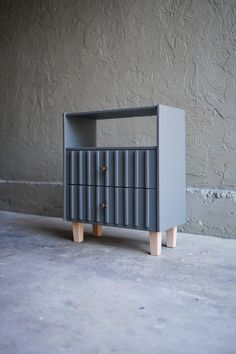 a grey cabinet with wooden legs on concrete floor