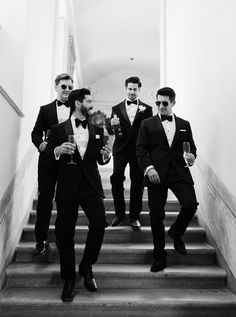 three men in tuxedos are walking down the stairs with wine glasses on their hands