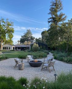 an outdoor fire pit surrounded by chairs and gravel in the middle of a garden area