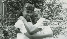 an old black and white photo of two people hugging each other in front of a bush