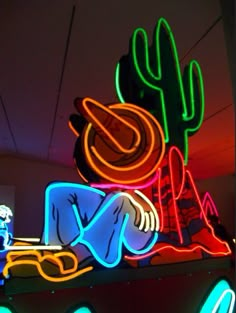 a neon sign with a person laying on the ground next to a cactus and some lights