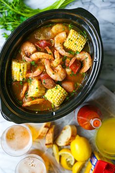 a crock pot filled with shrimp and corn on the cob next to orange juice