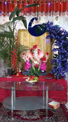 a glass table topped with lots of flowers next to a red cloth covered wall behind it