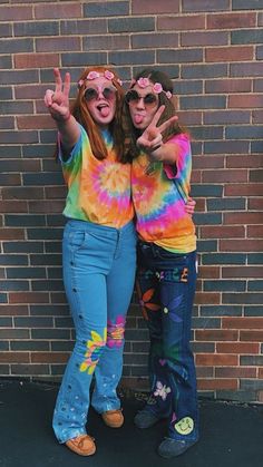 two young women standing next to each other in front of a brick wall with their hands up