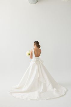 the back of a bride's dress as she stands in front of a white wall