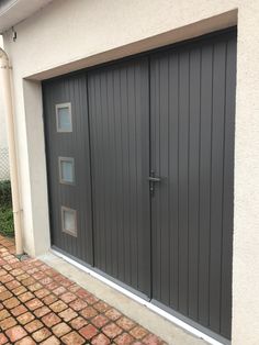 a garage door with two windows on the side of it and brick walkway next to it