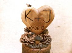 a wooden heart sitting on top of pine cones with the word kj written on it