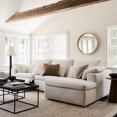 a living room with white couches and pillows on the floor in front of two windows