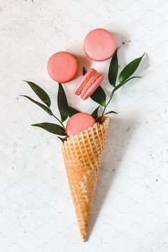 three pink macaroons in an ice cream cone with green leaves on the side