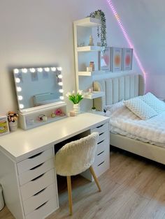 a bedroom with a bed, desk and mirror in the corner that has lights on it