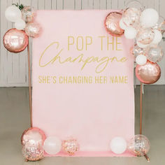 a pink and gold pop the champagne sign with balloons around it that says she's changing her name