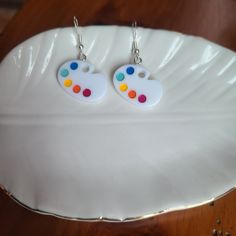 pair of white earrings with multicolored polka dots on them sitting on a plate