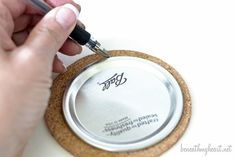 a person using a pen to write on a cork coaster