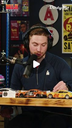 a man wearing headphones sitting in front of a wooden table with cars on it