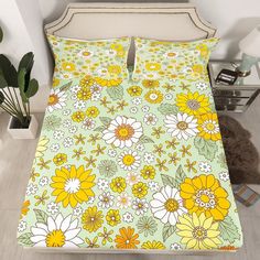 a bed with yellow and white flowers on the cover is next to a potted plant