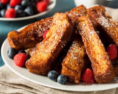 french toast with berries and powdered sugar on a plate next to bowls of fruit