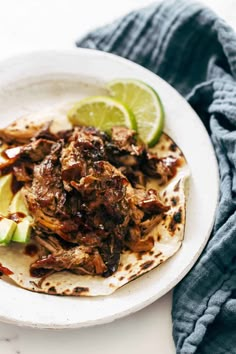 a close up of a plate of food with meat and limes on the side