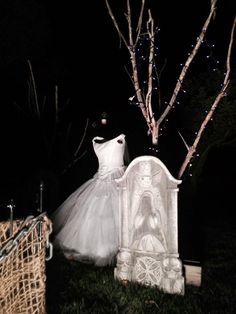 a white dress sitting on top of a bed next to a tree in the dark