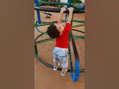 a young boy climbing up the side of a blue and green metal playground structure at a park