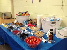 a blue table topped with lots of food and cups filled with fruit next to a bucket of ketchup