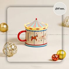 a cup with a carousel on it next to christmas ornaments