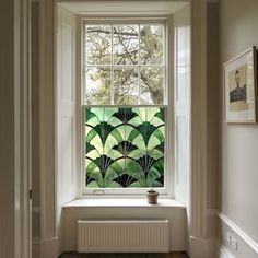 an open window with green leaves painted on the glass behind it in a white room