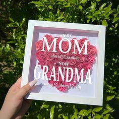 a hand holding up a framed paper heart with the words mom and grandma written on it