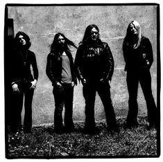 three men standing next to each other in front of a cement wall with long hair